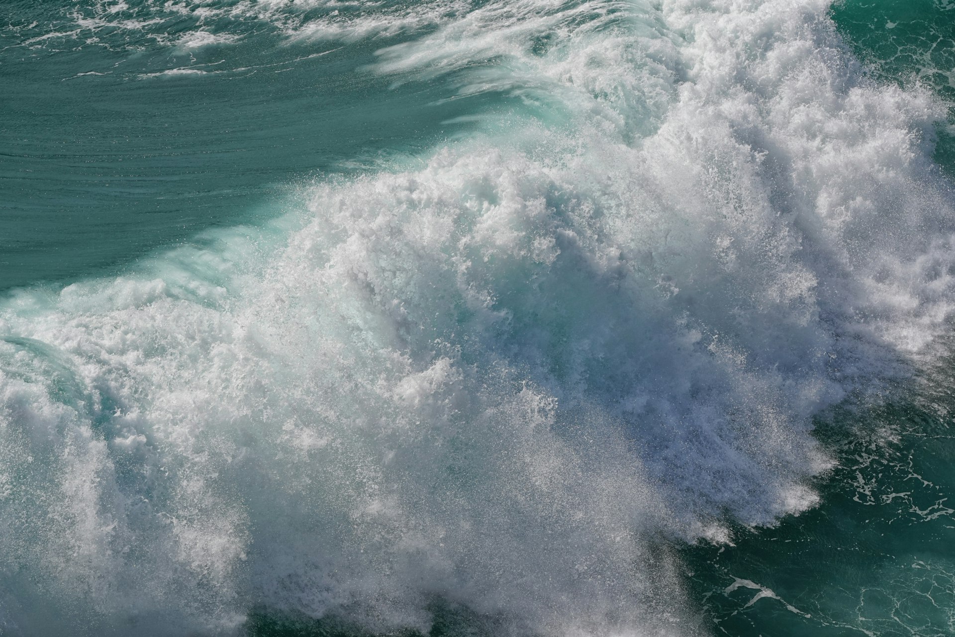 A large wave crashes with foamy water.